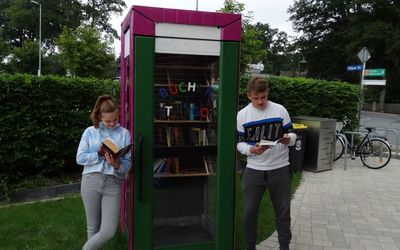 Die Schülerinnen und Schüler der Holzwerkstatt haben das Design und den Umbau der alten Telefonzelle komplett selbstständig geplant. Das Bild zeigt eine Schülerin und einen Schüler, die lesend vor der Tauschbibliothek stehen.
