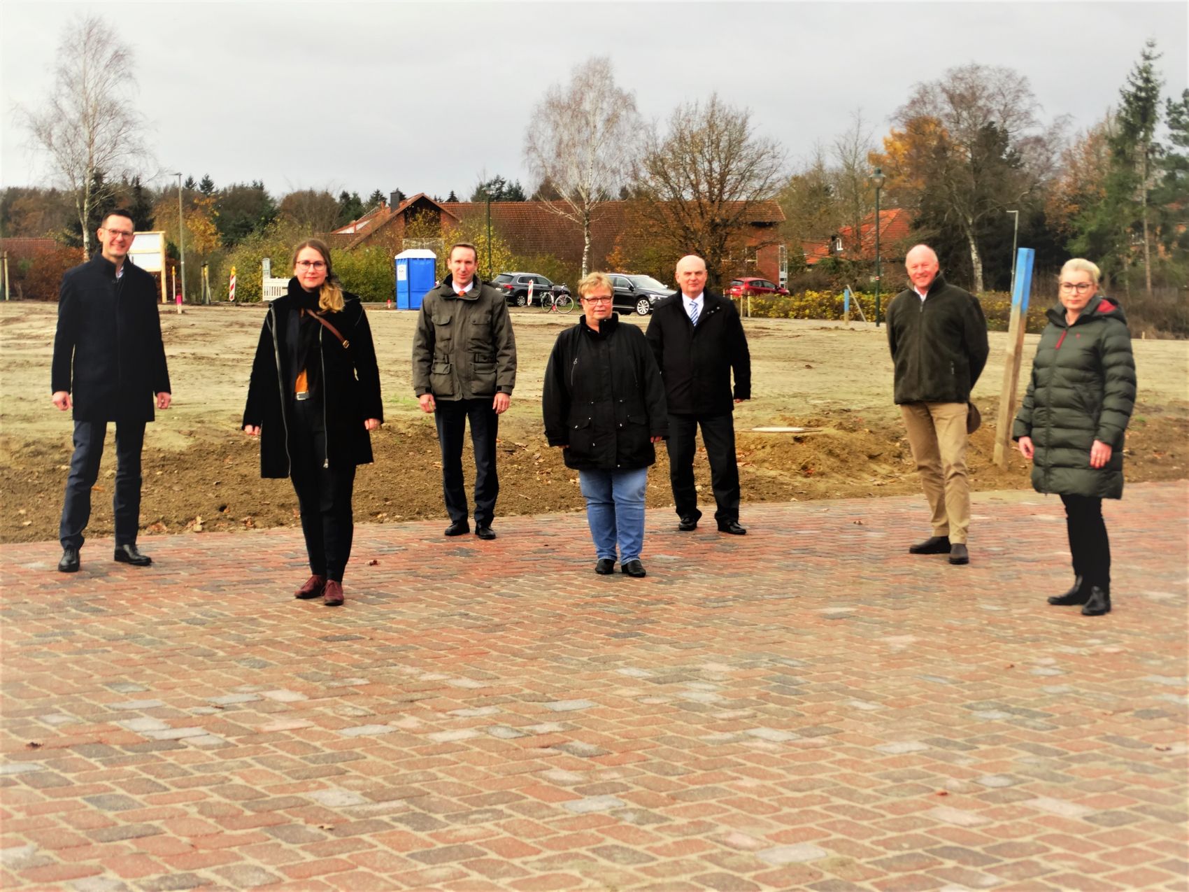 Fertigstellung Allermoor Das Foto zeigt eine Gruppe von Personen vor einem unbebauten Grundstück.