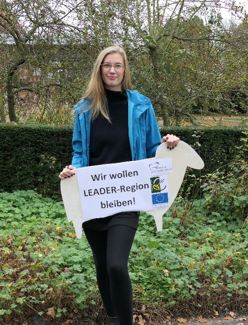 Das Foto zeigt Regionalmanagerin Lina Dening, die eine Pappheidschnucke in der Hand hält auf der steht