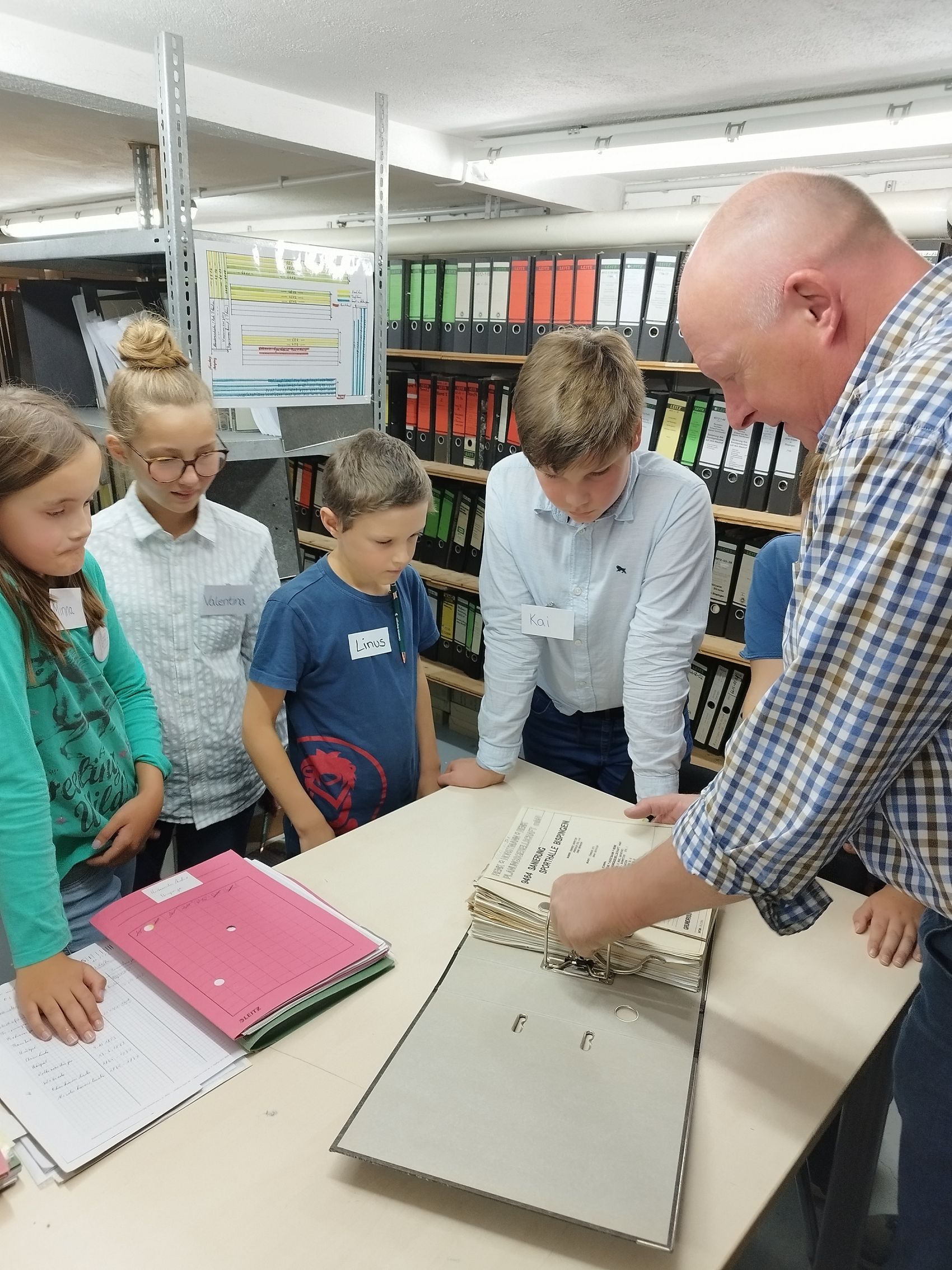 Bürgermeister Dr. Jens Bülthuis zeigt den Kindern das Rathaus. Das Bild zeigt Bürgermeister Dr. Jens Bülthuis und die Teilnehmenden der Kinderratssitzung, die um einen Tisch versammelt sind auf dem eine Akte liegt.