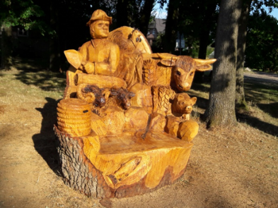 Holzskulptur von Volquard, dem Gründer des Dorfes, umgeben von Tieren. Die Skulptur zeigt detaillierte Darstellungen von Tieren und landwirtschaftlichen Elementen.