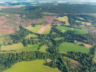 Luftbildaufnahme von Wilsede 2024, zeigt eine weitläufige Landschaft mit Wäldern, Feldern und landwirtschaftlichen Flächen in verschiedenen Grüntönen.