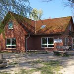 Backsteingebäude der Kita Hützel mit roten Dachziegeln, mehreren Fenstern und einer Holzbank im Vordergrund