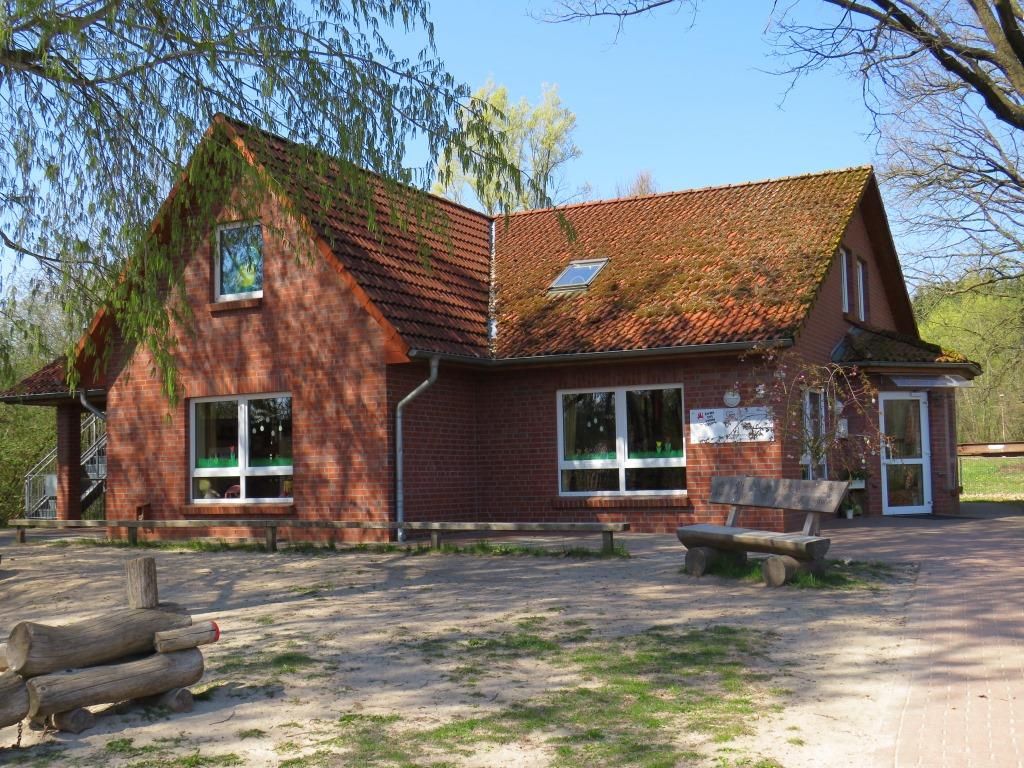 Backsteingebäude der Kita Hützel mit roten Dachziegeln, mehreren Fenstern und einer Holzbank im Vordergrund
