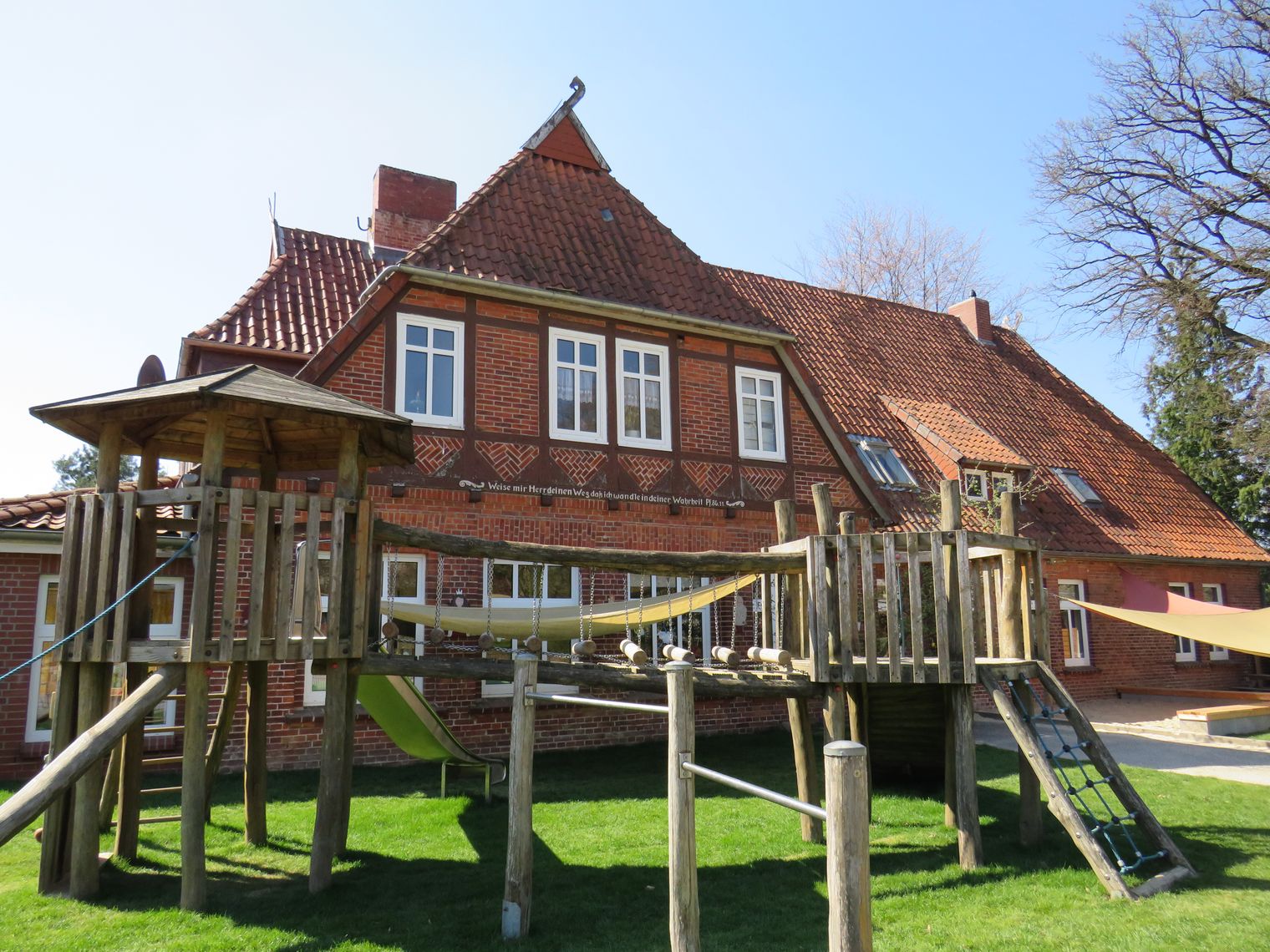 Backsteingebäude der Kita Behringen mit Spielplatz und Klettergerüst im Vordergrund