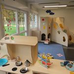 Innenansicht der Kita Wirbelwind mit Holzspielküche, Kletterwand mit bunten Griffen und verschiedenen Spielzeugen auf blauem Teppich