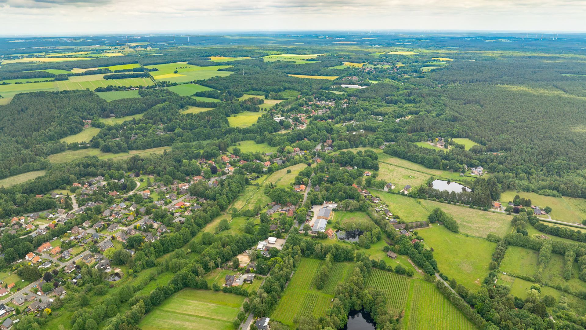 Luftbildaufnahme einer ländlichen Landschaft mit Feldern, Wäldern und verstreuten Wohngebieten. Sicht auf Huetzel 2024.