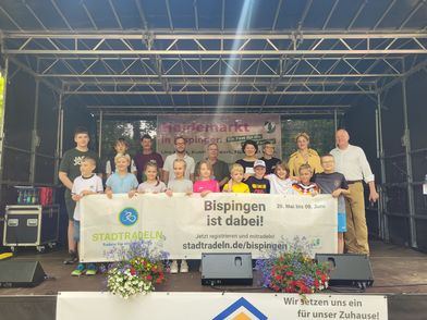 Gruppe von Kindern und Erwachsenen auf einer Bühne hält ein Banner mit der Aufschrift 'Bispingen ist dabei' und 'Stadtradeln' bei der Preisverleihung in Bispingen.