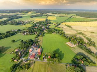 Luftbildaufnahme von Hoerpel 2024, zeigt eine weitläufige Landschaft mit Feldern, Wäldern und einem kleinen Ort im Vordergrund.