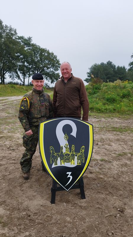 Oberstabsfeldwebel Klaffki und Bürgermeister Dr. Jens Bülthuis stehen vor einem Schild mit dem Wappen der Patenkompanie