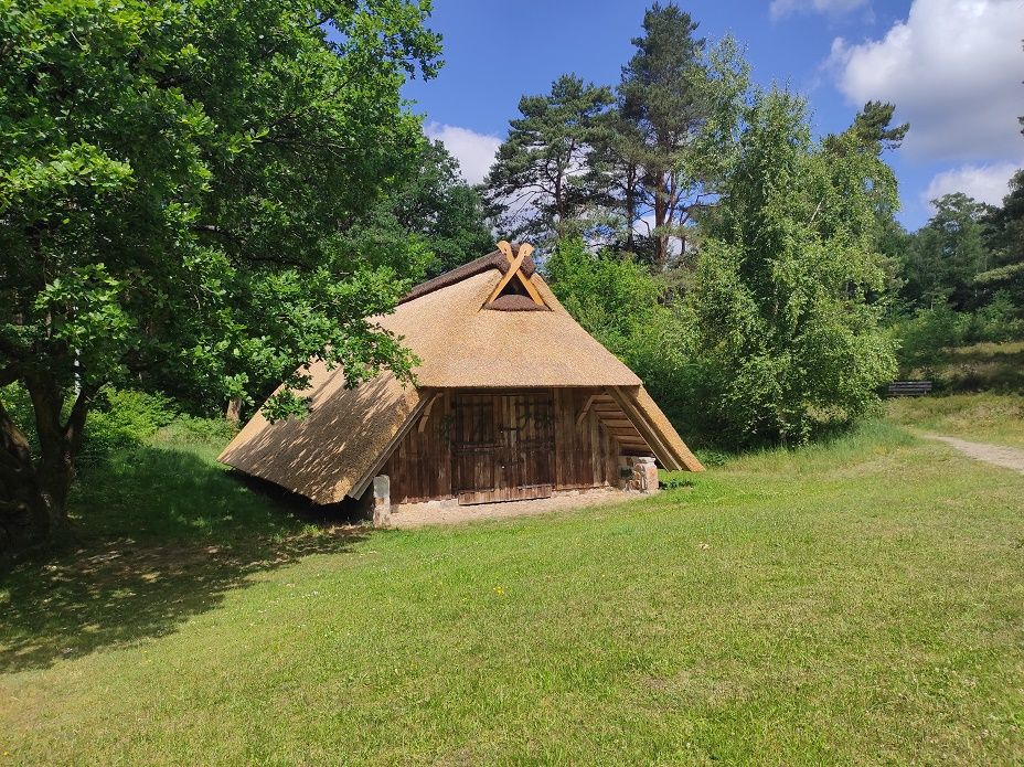 Traditioneller Schaftstall mit Reetdach im Heidjerpark, umgeben von Bäumen und Wiese