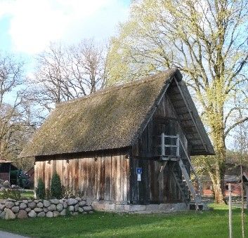 Treppenspeicher mit Reetdach in Volkwardingen, umgeben von Bäumen und Rasen. Das Gebäude hat eine Holzfassade und ein geneigtes Dach.