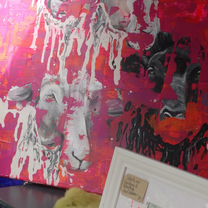 Gemaltes Bild mit abstrakten Tiergesichtern in Rot-, Weiß- und Schwarztönen, daneben grüne Blätter und ein weißer Bilderrahmen mit handgeschriebenem Zettel.