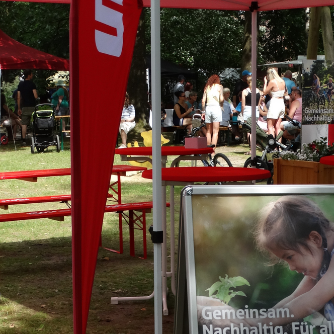 Rotes Werbebanner und Fahne der Kreissparkasse Soltau mit Text 'Gemeinsam für unsere Region.' auf einer Veranstaltung im Freien mit Tischen und Menschen im Hintergrund.