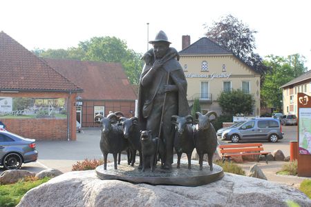 Schäferdenkmal in Bispingen zeigt einen Schäfer mit Hut und Mantel, umgeben von fünf Schafen auf einem Felsen