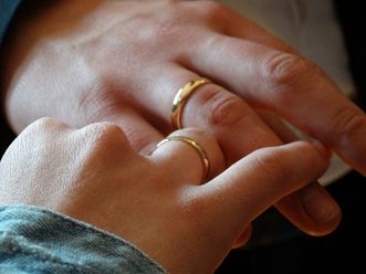 Zwei Hände mit goldenen Eheringen, die sich berühren