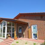 Eingang der Krippe Behringen mit rotem Backsteingebäude, Glasfenstern und Treppenstufen unter blauem Himmel