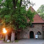 Ole Kerk Bispingen, kleine steinerne Kirche mit spitzem Ziegeldach, umgeben von Bäumen bei Sonnenuntergang