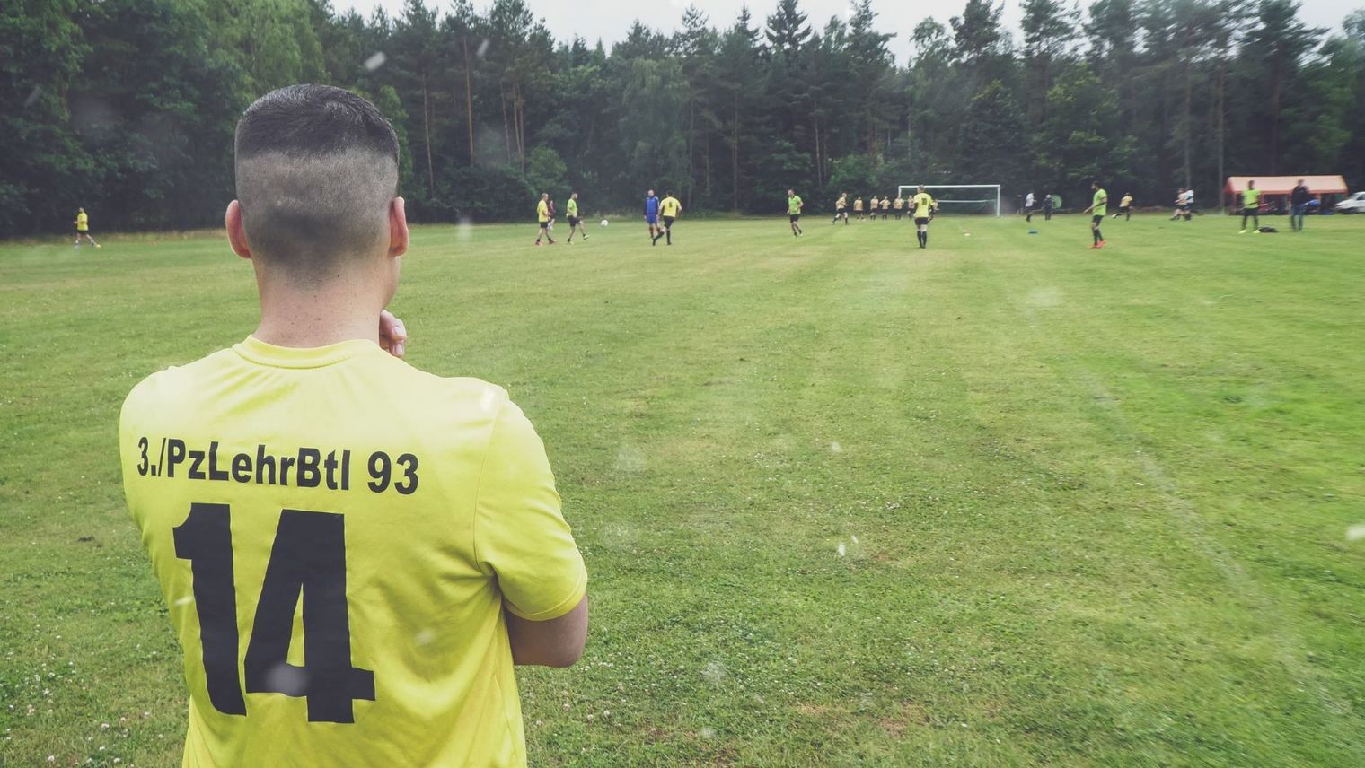 Spieler mit gelbem Trikot Nummer 14 vom 3. Panzerlehrbataillon 93 beobachtet Fußballspiel beim Firmenfußballpokalturnier auf Rasenplatz
