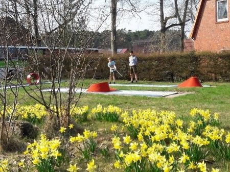 Zwei Kinder spielen Minigolf auf einer Anlage in Volkwardingen, umgeben von gelben Narzissen und Bäumen