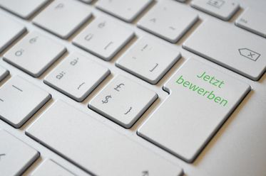 Weiße Computertastatur mit grüner Aufschrift 'Jetzt bewerben' auf der Enter-Taste