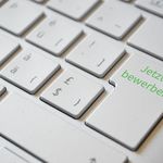 Weiße Computertastatur mit grüner Aufschrift 'Jetzt bewerben' auf der Enter-Taste
