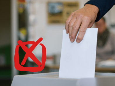 Hand legt weißen Wahlzettel in Wahlurne mit rotem Kreuzsymbol im Vordergrund