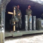 Zwei Soldaten in Tarnuniform stehen in einem mit Tarnnetz bedeckten Stand der Patenkompanie am Bispinger Heidemarkt mit Ausrüstung.