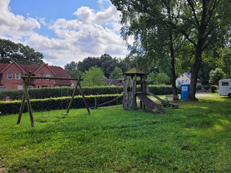 Spielplatz in Volkwardingen mit Schaukel, Kletterturm und Rutsche auf einer Wiese unter blauem Himmel mit Wolken