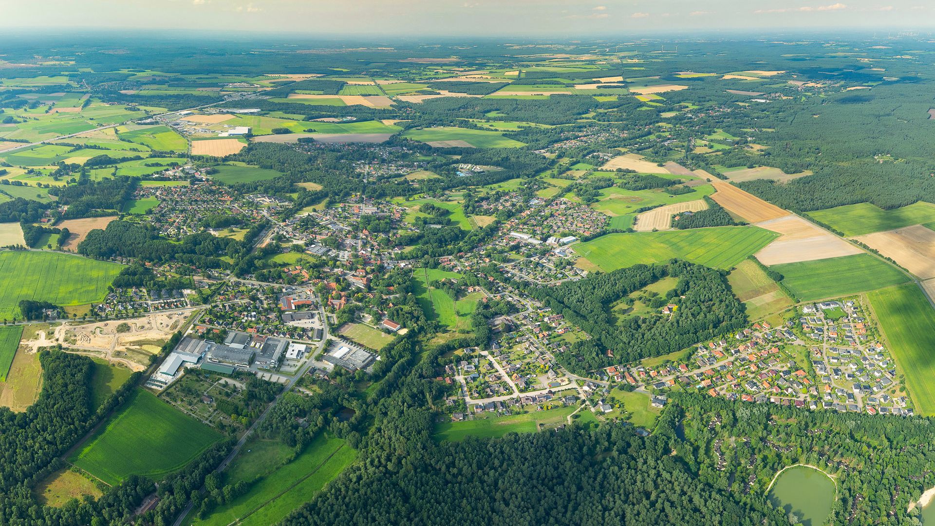 Luftbildaufnahme von Bispingen 2024, zeigt eine weitläufige Landschaft mit Wohngebieten, Feldern und Wäldern.