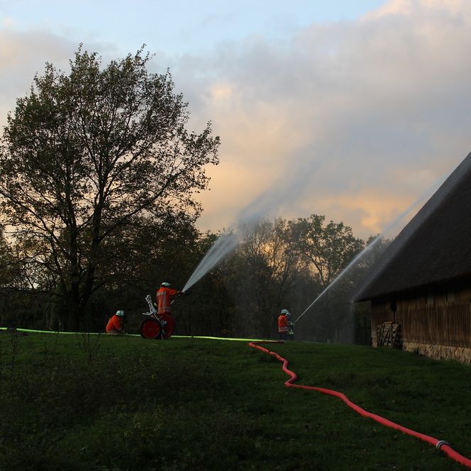 Feuerwehrübung im Heidetal mit Einsatzkräften, die Wasserstrahlen auf ein Gebäude mit Reetdach richten, um Brandbekämpfung zu trainieren